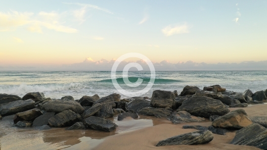 Waves Crashing Over Rocks on Sandy Beach